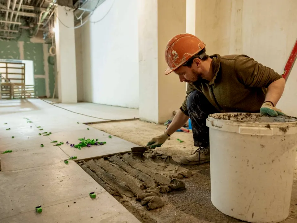 A tiler spreading adhesive with a notched trowel before laying large floor tiles